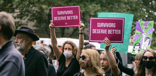 A person in a protest march holding up a sign that reads Justice for Survivors